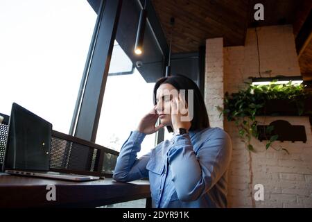 Donna freelance che ha emicrania al caffè. Giovane donna che lavora nella caffetteria davanti al computer portatile e soffre di mal di testa croniche quotidiane. Concetto di stipendio malato Foto Stock