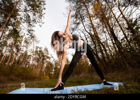 Donna che fa yoga o pilates esercizio. In piedi in posizione yoga triangolo. Concetto di stile di vita sano. Allenati all'aperto. Giovane donna in reggiseno nero e. Foto Stock