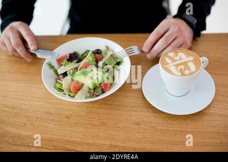 Ora di pranzo lavoratore maschile mangiare il suo pasto delizioso e sano. Uomo gustando insalata e piatto bianco. Prendetevi cura di voi stessi e non dimenticate di mangiare prima Foto Stock