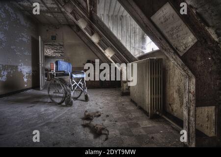 Una vecchia sedia a rotelle in una camera in rovina con pareti sporche di un edificio abbandonato Foto Stock