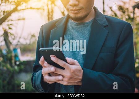 Uomo d'affari che tiene in mano lo smartphone mobile e che tocca sullo schermo Foto Stock