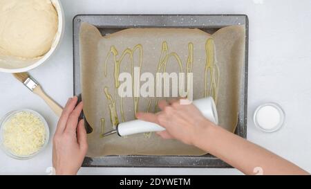 Lo chef versa l'olio d'oliva su una teglia da forno. Cottura del pane piatto, vista ravvicinata dall'alto Foto Stock