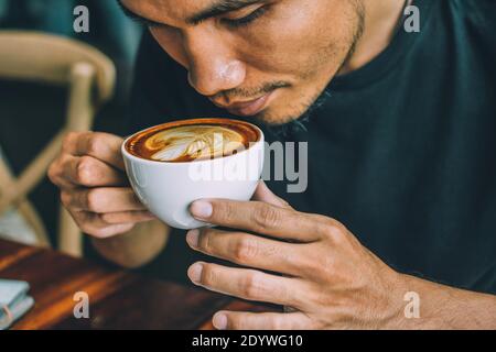 Tenere una tazza di latte di caffè e bere caffè Foto Stock