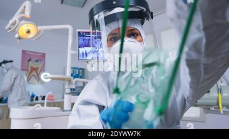 Dentista in tuta appoggiato su paziente che mette maschera di oxigen prima di chirurgia in ufficio stomatologico con nuovo normale. Stomatolog indossare gli attrezzi di sicurezza contro il covid19 durante il controllo di heatlhcare della persona. Foto Stock