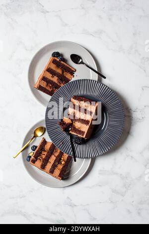 Pezzi di torta al cioccolato con frutti di bosco su un piatto grigio, sfondo di marmo bianco. Concetto di dessert vegano. Foto Stock