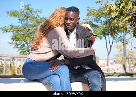 Uomo nero africano e rosso donna caucasica abbracciando con una rosa. Giovane coppia multirazziale che celebra il giorno delle valentine. Foto Stock