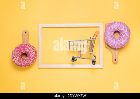 Due ciambelle con glassa di zucchero rosa e cosparse di coloratissime briciole di pasticceria, su sfondo giallo. Il concetto di shopping Foto Stock