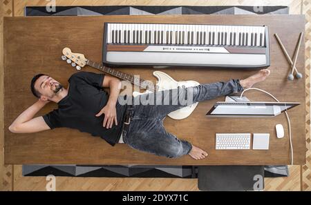 Composizione vista dall'alto con strumenti musicali su un grande tavolo di legno e un uomo. Concetto di creatività musicale. Foto Stock