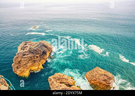 Vista dall'alto delle onde che infrangono le scogliere e le piccole isole di roccia nelle acque turchesi azzurre dell'Oceano Atlantico vicino alla città di Nazare, orizzonte infinito di Atlant Foto Stock