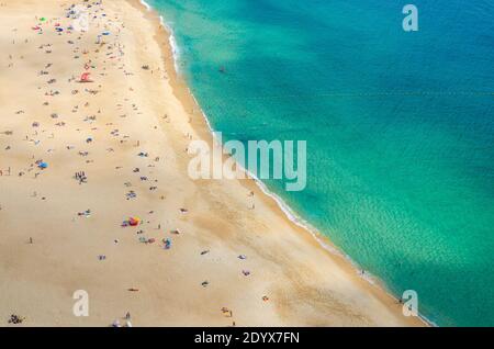 Vista dall'alto della spiaggia di sabbia con i turisti che prendono il sole e le acque turchesi azzurre dell'Oceano Atlantico, Praia da Nazare costa cittadina con le onde, le Foto Stock
