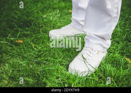 Piedi maschi in scarpe bianche su erba verde. Jeans bianchi. Foto Stock