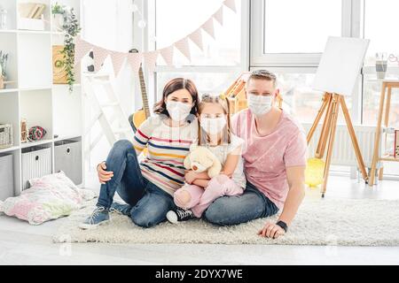 Bella famiglia che indossa maschere mediche seduto sul pavimento in bambini camera Foto Stock