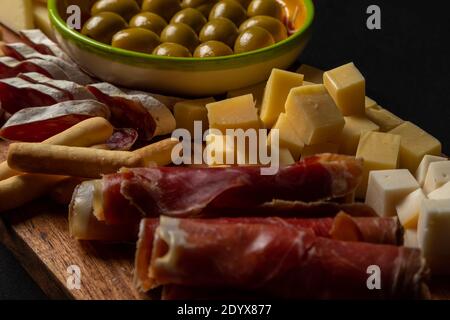 Piatto di tapas spagnole su un vassoio di legno rustico con una varietà di formaggi, carne tipica e pane Foto Stock