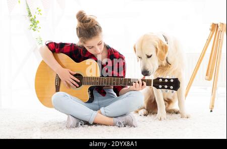 ragazza adolescente che suona la chitarra con il cane carino a casa Foto Stock