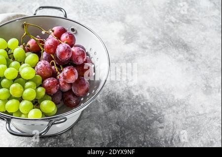 Due varietà di uve, rosso e verde in un colander. Sfondo grigio. Vista dall'alto. Spazio di copia Foto Stock