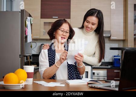 Donna asiatica anziana e sua figlia adulta che discute le bollette di utilità hanno bisogno di pagare in linea quando si siede al tavolo della cucina Foto Stock