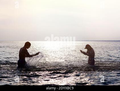 Silhouette di due persone con spruzzi in acqua sul Tramonto sfondo Foto Stock