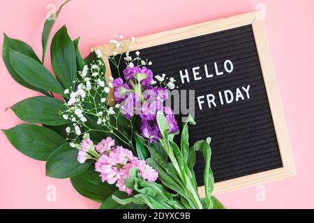 Ciao testo del venerdì sulla lavagna nera e bouquet fiori colorati su sfondo rosa. Concetto Happy Friday. Modello per cartolina, biglietto d'auguri Fl Foto Stock