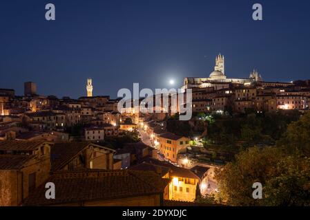 Luna piena su un vicolo illuminato e il panorama del centro storico medievale di Siena con la cattedrale, la torre dell'orologio del municipio, la Toscana, l'Italia Foto Stock