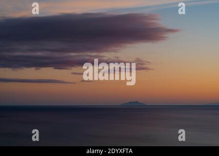 Nuvole colorate sull'isola di Montechristo nel Mar Tirreno al largo della costa toscana al tramonto, Maremma, Italia Foto Stock