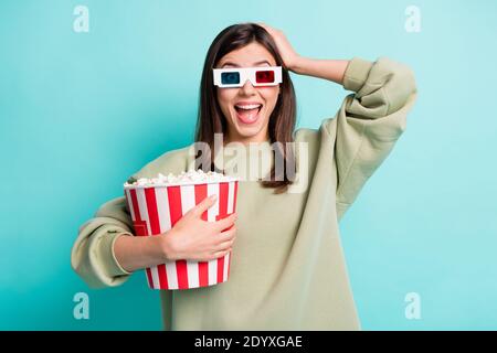 Ritratto fotografico di una donna scioccata in occhiali 3d che toccano la testa tenendo la benna di popcorn gigante in una mano isolata su vivace sfondo colorato Foto Stock