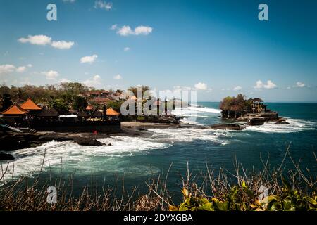 Tempio Tanah Lot nell'oceano ondulato e nei ristoranti sulla costa Foto Stock