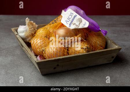 ZUTPHEN, PAESI BASSI - 16 dicembre 2020: Ancora vivo low key studio shot di legno contenitore vassoio cassa con cipolle in una rete e aglio su una cucina rustica Foto Stock