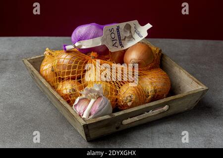 ZUTPHEN, PAESI BASSI - 16 dicembre 2020: Ancora vivo low key studio shot di legno contenitore vassoio cassa con cipolle in una rete e aglio su una cucina rustica Foto Stock