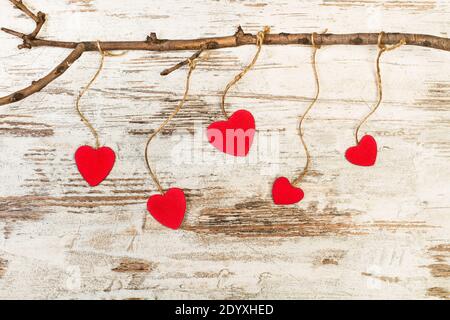 Cuori di carta rossi appesi da un ramo su un legno tabella Foto Stock