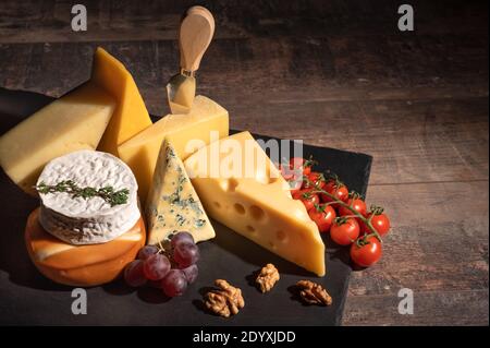 vari tipi di formaggio su tavola rustica in legno. Piatto di formaggio: Parmigiano, cheddar, gouda, camembert, brie con noci su tavola di legno su sfondo scuro w Foto Stock