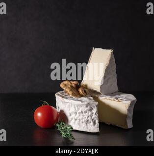 Delizioso formaggio brie con pomodoro e noce su sfondo nero. Tipo Brie di formaggio. Camembert. Formaggio Brie fresco e una fetta su tavola di pietra. Italia Foto Stock