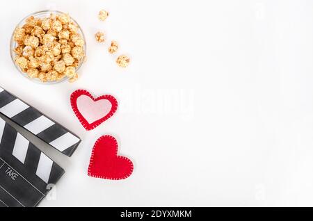 Concetto di film di San Valentino. Clapperboard con cuori e popcorn caramello con spazio di copia su sfondo bianco. Foto Stock