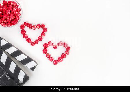 Concetto di film di San Valentino. Clapperboard con cuori di popcorn rosso caramello con spazio di copia su sfondo bianco. Foto Stock