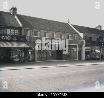 Anni '1960, storica, una strada principale britannica che mostra una vista esterna di un nuovo punto vendita per il Post Office, Inghilterra, Regno Unito. Una signora con una carrozza costruita su carrozza sta guardando nella finestra del negozio accanto, un negozio di scarpe o quello che in quest'epoca veniva chiamato, un negozio di calzature. Foto Stock