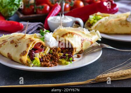 pancake abbondante con carne e verdure piccanti ripieno su un piatto bianco con forchetta su tavolo da cucina. tagliato aperto Foto Stock