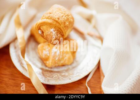 Croissant freschi croccanti in un piatto d'argento su un legno tavolo con tela bianca e nastri Foto Stock
