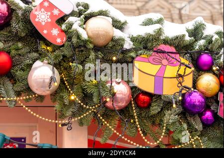 primo piano della decorazione festosa della città di natale. brunch all'albero fure coperto di neve decorata con baubles e ghirlande. Foto Stock