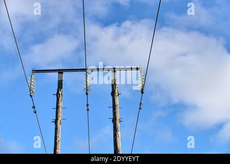 Linee elettriche aeree sul vecchio pilastro in legno catturate contro il cielo blu con nubi bianche soffici in Co. Dublino, Irlanda. Tre fili di tensione Foto Stock