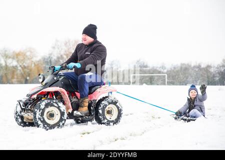 Kidderminster, Regno Unito. 28 dicembre 2020. Tempo nel Regno Unito: Dopo una significativa nevicata in tutto il Worcestershire questa mattina, le famiglie si presentano con idee nuove per intrattenere i loro bambini. Qui abbiamo un ragazzino che viene trainato dietro una moto quad mentre ci si siede a bordo di un coperchio della pattumiera! Credit: Lee Hudson/Alamy Live News Foto Stock