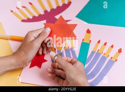 Una ragazza fa una carta per Hanukkah felice con le sue mani, un candelabro e candele sulla carta Foto Stock