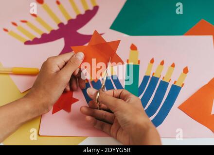 Una ragazza fa una carta per Hanukkah felice con le sue mani, un candelabro e candele sulla carta Foto Stock