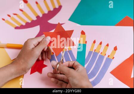 Una ragazza fa una carta per Hanukkah felice con le sue mani, un candelabro e candele sulla carta Foto Stock