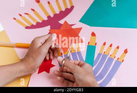 Una ragazza fa una carta per Hanukkah felice con le sue mani, un candelabro e candele sulla carta Foto Stock