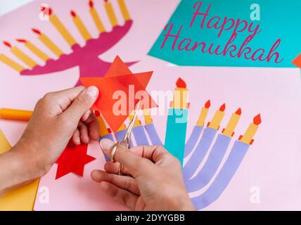 Una ragazza fa una carta per Hanukkah felice con le sue mani, un candelabro e candele sulla carta Foto Stock