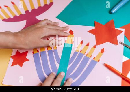 Una ragazza fa una carta per Hanukkah felice con le sue mani, un candelabro e candele sulla carta Foto Stock