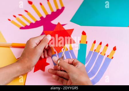 Una ragazza fa una carta per Hanukkah felice con le sue mani, un candelabro e candele sulla carta Foto Stock