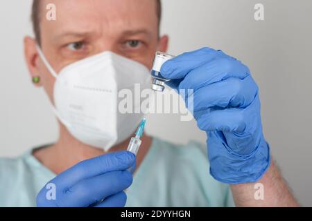 Infermiere di sesso maschile con maschera facciale e guanti blu, contenente siringa con ago e flaconcino di vaccino covid-19. Concetto medico. Foto Stock