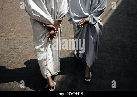 Indietro vista di due uomini vestiti di djellaba marocchina radiotiva che camminano sulla strada di Marrakech , Marocco . Foto Stock