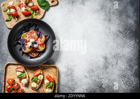 Insalata caprese assortita, spiedini, tartine, bruschette con pomodori ciliegini, mozzarella e basilico. Sfondo grigio. Vista dall'alto. Spazio di copia Foto Stock