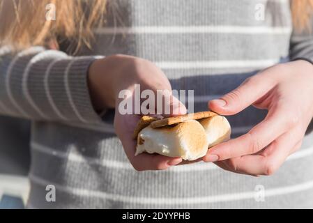 Primo piano delle mani della donna che tengono s'More fatti sopra un fuoco il giorno di sole Foto Stock